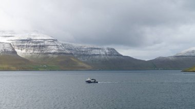 Faroe Adaları 'ndaki dramatik manzarada yelken açan balıkçı teknesi.