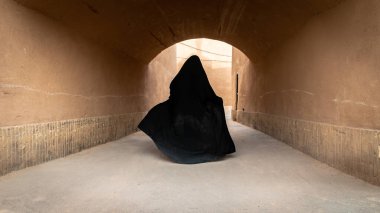 İran 'ın Yazd kentinin dar sokaklarında siyah tesettüre bürünmüş kimliği belirsiz Müslüman bir kadın yürüyor..