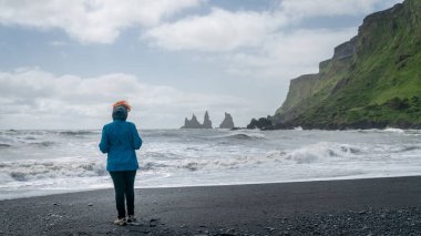 İzlanda, Vik 'in güney kıyısındaki Reynisfjara' nın siyah kumsalındaki kimliği belirsiz kadın..
