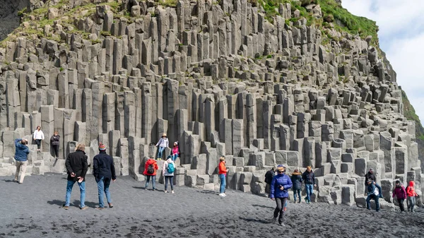 Touristen besuchen den schwarzen Sandstrand von Reynisfjara und die Basaltsäulen an der Südküste Islands. — Stockfoto