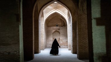 İran 'ın İsfahan kentindeki Jameh Camii' nin antik sütunları boyunca yürüyen siyah tesettürlü kimliği belirsiz İranlı kadın.