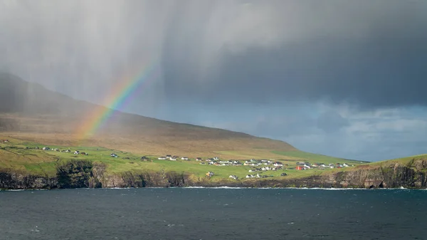 Dramatisch landschap op de Faeröer met traditionele huizen onder regenboog in het noorden van de Atlantische Oceaan — Stockfoto