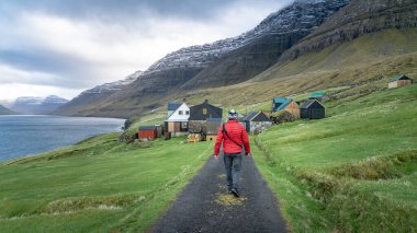 Kuzey Atlantik 'teki geleneksel evlerle Faroe Adaları' nda dramatik manzaralarda yürüyen kimliği belirsiz bir adam.