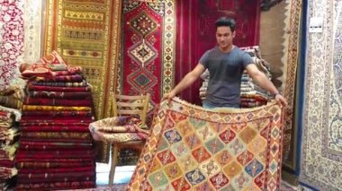 İsfahan, İran - Mayıs 2019: Genç İranlı halı satıcısı bir halı dükkanında turistlere İran halıları sundu