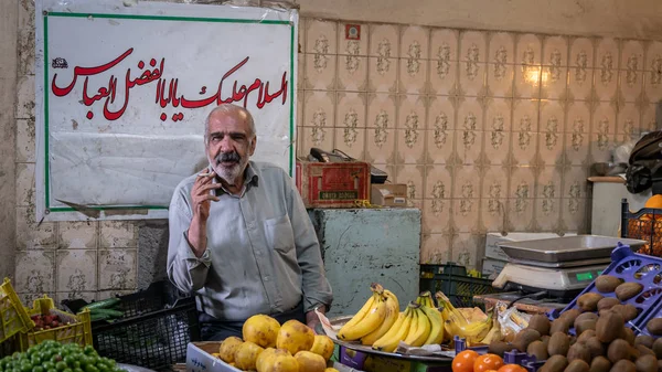 Iráni zöldséges cigarettázik, miközben gyümölcsöt árul az iszfaháni Grand Bazaarban, Iránban. — Stock Fotó