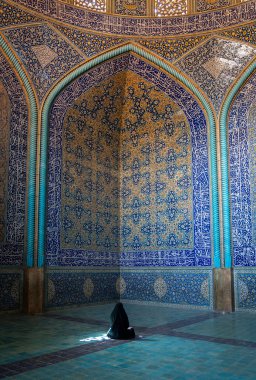 İsfahan, İran - Mayıs 2019: Kimliği belirsiz İranlı kadın çarşaf giyip Şeyh Lotfollah Camii 'nin içinde duvarlarında fayanslarla dua ediyor, İsfahan, İran