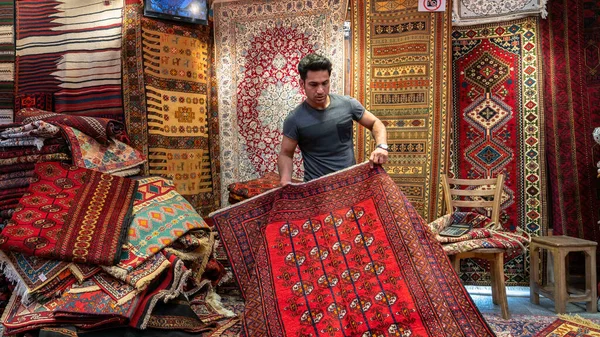 İsfahan, İran - Mayıs 2019: Genç İranlı halı satıcısı bir halı dükkanında turistlere İran halıları sundu