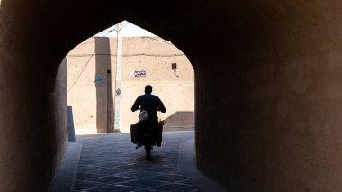 Yazd, İran - Mayıs 2019: İran 'ın Yazd kentinin dar sokaklarında motosikletli bir adam.