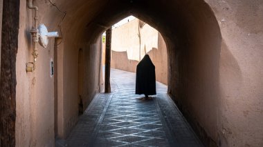 Yazd, İran - Mayıs 2019: İran 'ın Yazd kentinin dar sokaklarında siyah tesettüre bürünmüş, kimliği belirsiz Müslüman kadın.