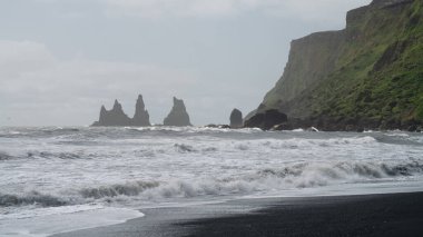 Reynisfjara 'nın siyah kumlu sahili. Denizde kaya oluşumları var. İzlanda' nın güney kıyısında.