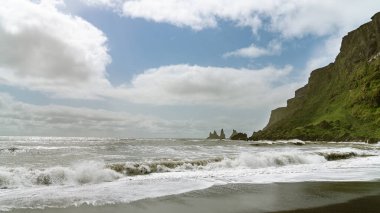 Reynisfjara 'nın siyah kumlu sahili. Denizde kaya oluşumları var. İzlanda' nın güney kıyısında.