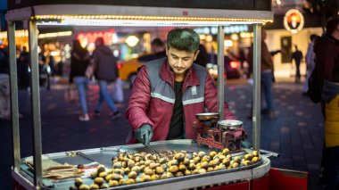 İstanbul, Türkiye - Kasım 2019: Taksim ilçesinde kestane satan bir adam, İstanbul 'un Istiklal Caddesi' nde kalabalık insanlarla yürüyor