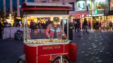 İstanbul, Türkiye - Kasım 2019: Taksim ilçesinde kestane satan bir adam, İstanbul 'un Istiklal Caddesi' nde kalabalık insanlarla yürüyor