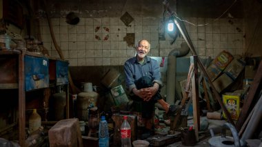 Yazd, İran - Mayıs 2019: Yaşlı İranlı bir adam dükkanındaki taburede çeşitli eski aletlerle oturuyor