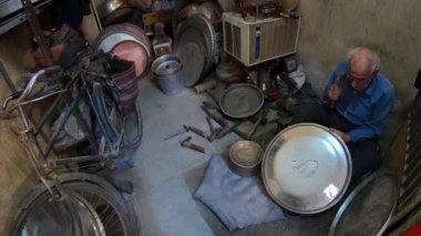 Yazd, İran - Mayıs 2019: Yaşlı İranlı adam çekiçle çeşitli eski aletlerle bir mağazada çalışıyor