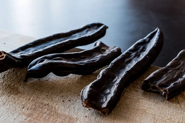 Rijpe peulen van johannesbrood op houten oppervlak. — Stockfoto