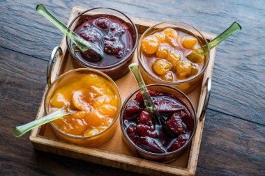 Çeşitli cam kase meyve kayısı, kiraz, çilek, damson Erik reçel içinde ahşap tepsi.