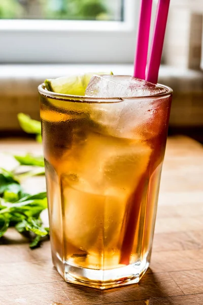 Long island iced tea cocktail with lime, ice and served with pink straw