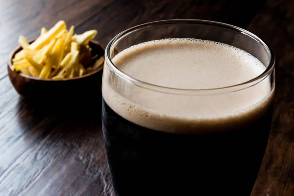 Cerveza oscura con bocadillos patatas fritas en la superficie de madera . — Foto de Stock