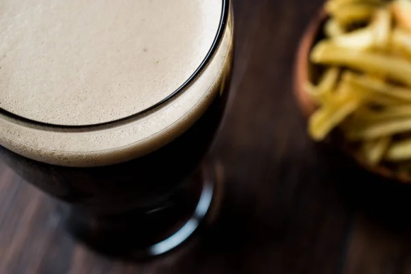 Birra scura con snack patatine sulla superficie di legno . — Foto Stock