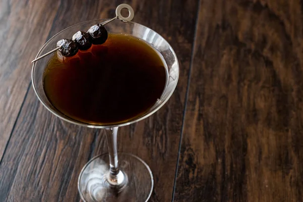 Cocktail Manhattan noir aux olives sur une surface en bois sombre . — Photo
