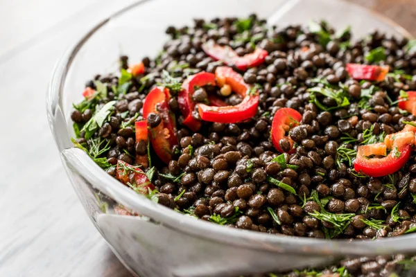 Salade de lentilles noires aux poivrons rouges et persil dans un bol en verre . — Photo