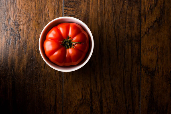 Big Tomato in bowl on wooden surface.