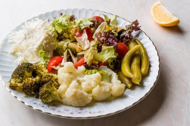 Karnabahar, kereviz, brokoli, turşu, domates ve limon ile sebze tabağı.