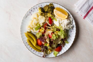 Karnabahar, kereviz, brokoli, turşu, domates ve limon ile sebze tabağı.