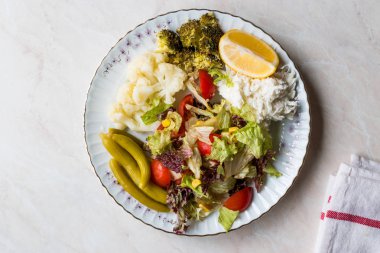 Karnabahar, kereviz, brokoli, turşu, domates ve limon ile sebze tabağı.