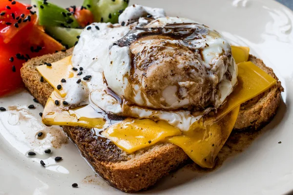 Uova in camicia su pane tostato con formaggio Cheddar, aceto balsamico, insalata e semi di sesamo nero o cumino . — Foto Stock