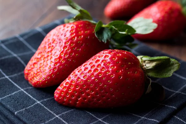 Fresas frescas orgánicas maduras dos con hojas en la superficie oscura con mantel . — Foto de Stock