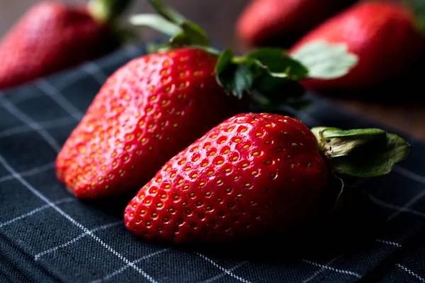 Fresas frescas orgánicas maduras dos con hojas en la superficie oscura con mantel . — Foto de Stock