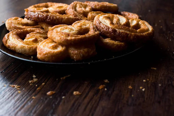 Palmier Cookies in zwarte plaat op houten oppervlak. — Stockfoto