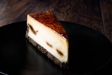 Koyu ahşap yüzeye sahip siyah plaka üzerinde kahve Cheesecake.