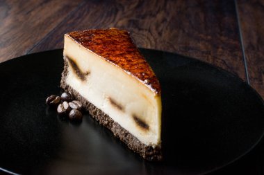 Koyu ahşap yüzeye sahip siyah plaka üzerinde kahve Cheesecake.