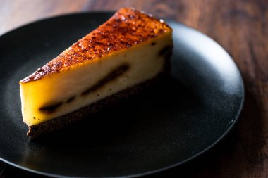 Koyu ahşap yüzeye sahip siyah plaka üzerinde kahve Cheesecake.