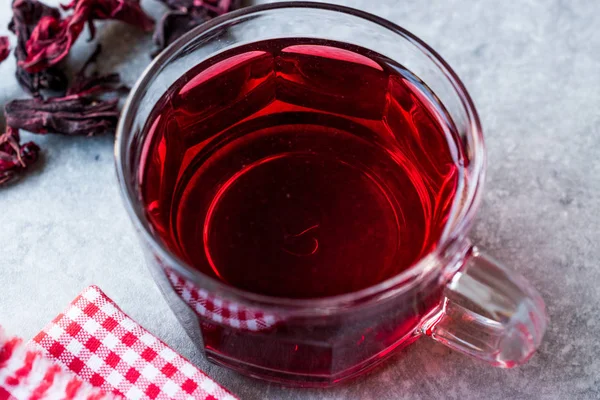 Thé chaud rouge d'hibiscus dans une tasse en verre avec des feuilles de thé sèches d'hibiscus — Photo