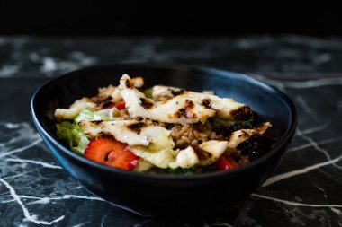 Izgara Halloumi Peynir Salatası ve Çilek Dilimleri ve Karabuğday / Hellim in Black Bowl on Dark Granite Surface. Organik Taze Yiyecek.