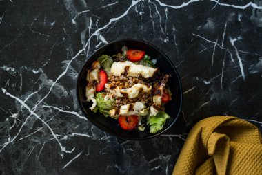 Izgara Halloumi Peynir Salatası ve Çilek Dilimleri ve Karabuğday / Hellim in Black Bowl on Dark Granite Surface. Organik Taze Yiyecek.
