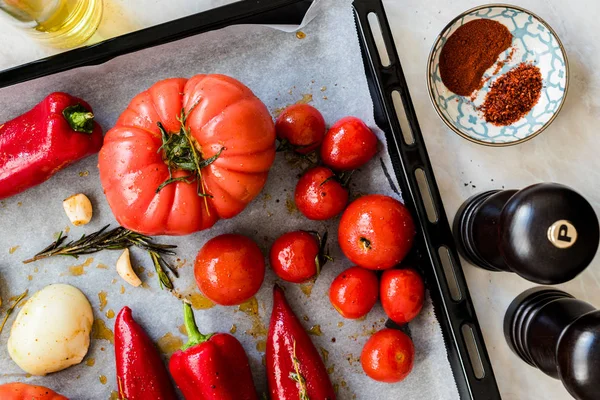 Pieczone pomidory, czerwona papryka, cebula, pomidory wiśniowe, przyprawy, rozmaryn i młyn solny z tacą do pieczenia i papieru arkuszowego. Żywność ekologiczna. — Zdjęcie stockowe