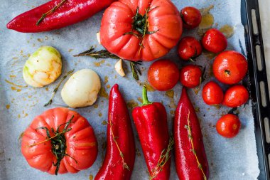 Kızarmış domatesler, kırmızı biberler, soğanlar, kiraz domatesleri, baharatlar, biberiye ve biberiye ile fırın tepsisi ve çarşaf kağıdı. Organik Gıda.