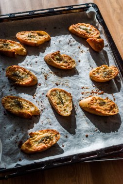 Sarımsaklı Parmesan peyniri ekmek dilimleri fırın tepsisiyle kağıt çarşaf üzerinde.