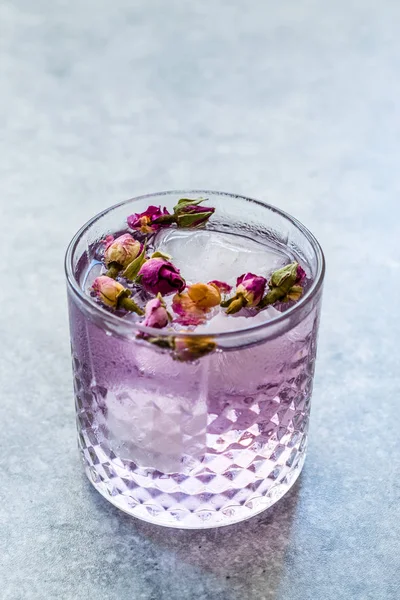 Розовый джин тоник коктейль с сушеными бутонами роз и льдом в стеклянном кубке . — стоковое фото