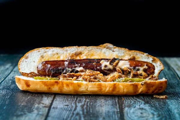 Hot dog s karamelizovanou cibulí, čedarem a sýrovou omáčkou Gruyere na dřevěném povrchu s bramborami. Fast Food. — Stock fotografie