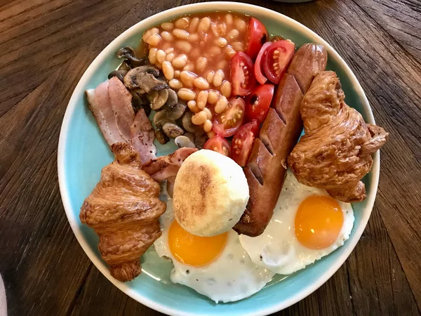 Englisches Frühstück mit Würstchen, gegrillten Tomaten und Pilzen, Ei, Speck, gebackenen Bohnen und kleinen Mini-Croissants. traditionelle Mahlzeit. — Stockfoto