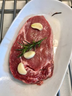 Zeytinyağı, sarımsak ve biberiyeyle marine edilmiş çiğ biftek. Pişirilmeye hazır. Organik Gıda.