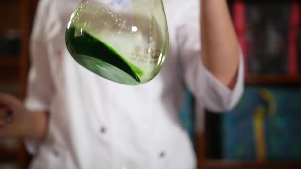 Vědec v bílém plášti drží skleněnou baňku pro experimenty a míchá zelenou tekutinu. Zpomalení. dva snímky v záběru — Stock video