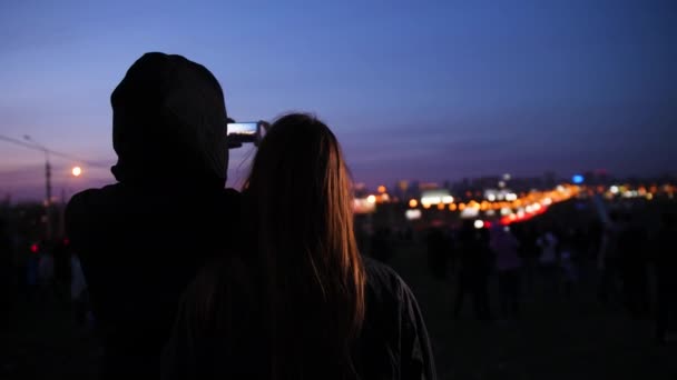 Un chico y una chica miran la vista nocturna de la ciudad y toman fotos — Vídeos de Stock