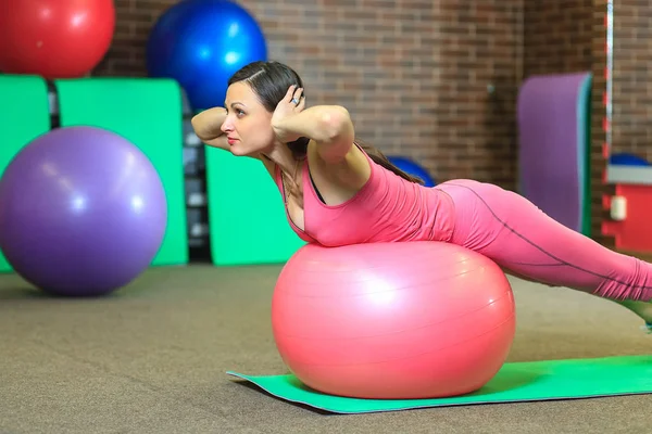 Junge schöne weiße Mädchen in einem rosa Sportanzug macht körperliche Übungen mit einem fitten Ball. — Stockfoto